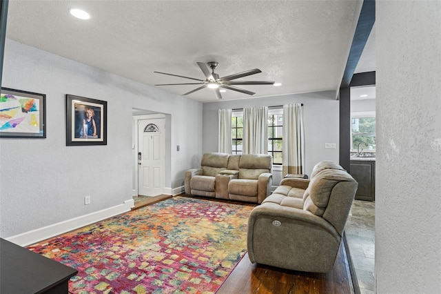 living area with a textured ceiling, a textured wall, ceiling fan, and wood finished floors
