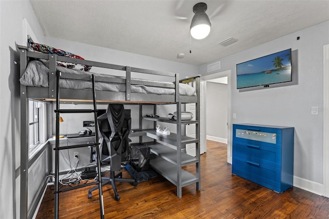 bedroom with visible vents, a textured ceiling, baseboards, and wood finished floors