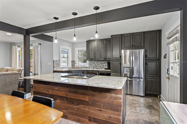 kitchen with appliances with stainless steel finishes, hanging light fixtures, tasteful backsplash, a center island, and light stone counters