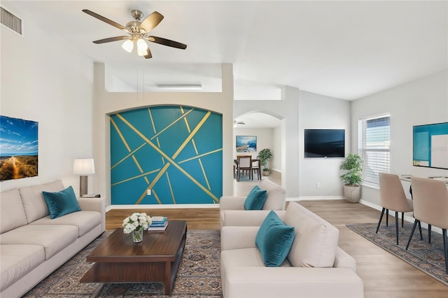 living room featuring arched walkways, a ceiling fan, baseboards, wood finished floors, and visible vents