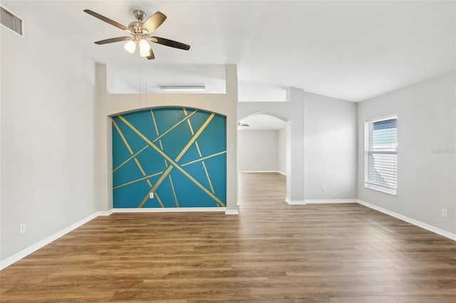 spare room with arched walkways, a ceiling fan, baseboards, wood finished floors, and visible vents