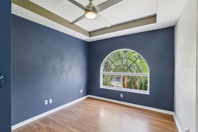 empty room featuring baseboards, ceiling fan, a tray ceiling, and wood finished floors