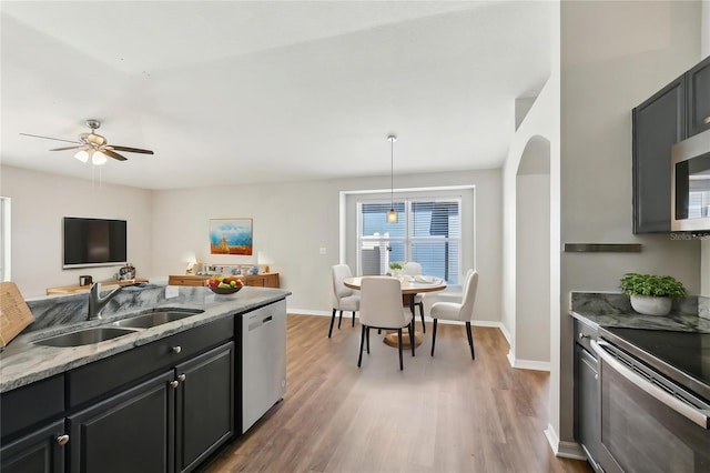 kitchen featuring ceiling fan, appliances with stainless steel finishes, wood finished floors, a sink, and light stone counters