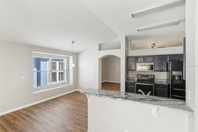 kitchen featuring arched walkways, appliances with stainless steel finishes, wood finished floors, and a breakfast bar
