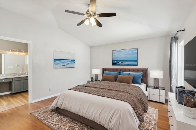 bedroom featuring light wood-style floors, ensuite bathroom, ceiling fan, a sink, and vaulted ceiling