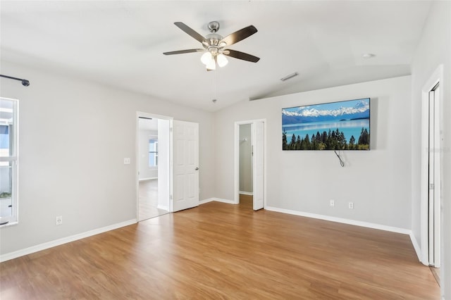 unfurnished bedroom featuring a ceiling fan, visible vents, vaulted ceiling, wood finished floors, and baseboards