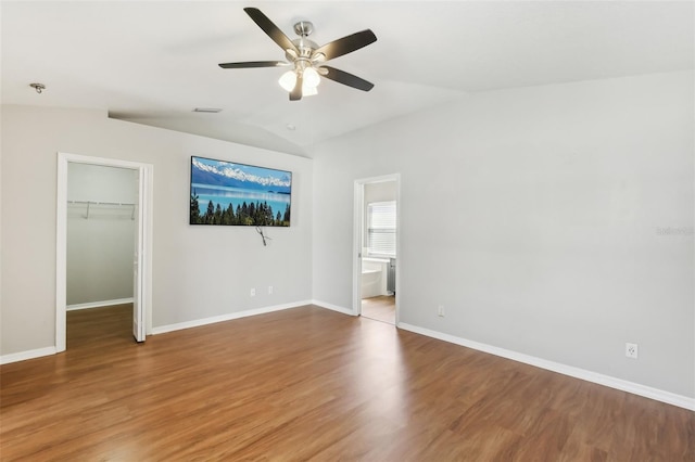 unfurnished bedroom featuring vaulted ceiling, wood finished floors, baseboards, a closet, and a spacious closet