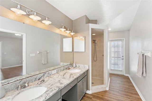full bathroom featuring a sink, double vanity, a tile shower, and wood finished floors