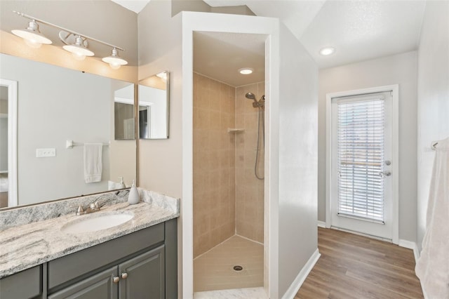 bathroom featuring baseboards, vanity, tiled shower, and wood finished floors