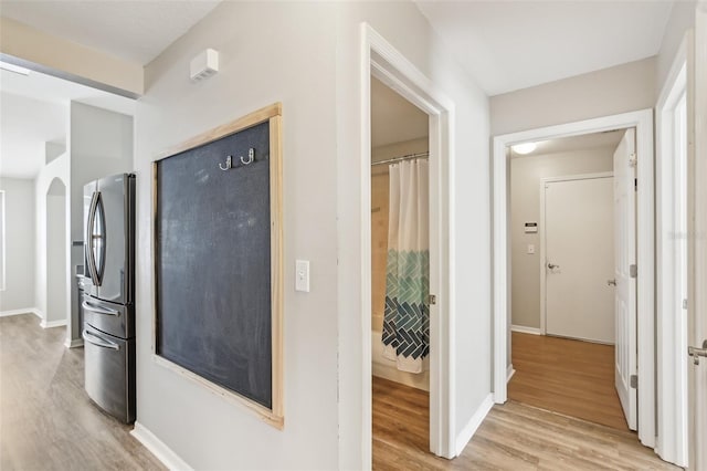 hallway with light wood-style floors, baseboards, and arched walkways