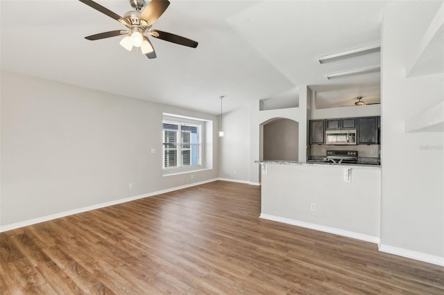 unfurnished living room featuring a ceiling fan, arched walkways, wood finished floors, baseboards, and lofted ceiling