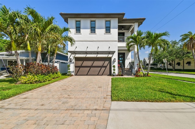 view of front facade with a front yard, decorative driveway, a balcony, an attached garage, and stucco siding