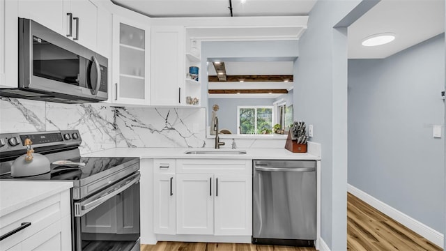 kitchen with appliances with stainless steel finishes, a sink, light countertops, light wood-style flooring, and backsplash