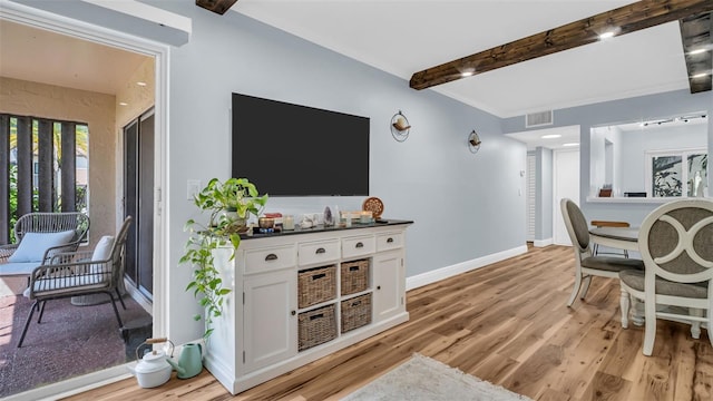 interior space with baseboards, light wood finished floors, beam ceiling, and visible vents