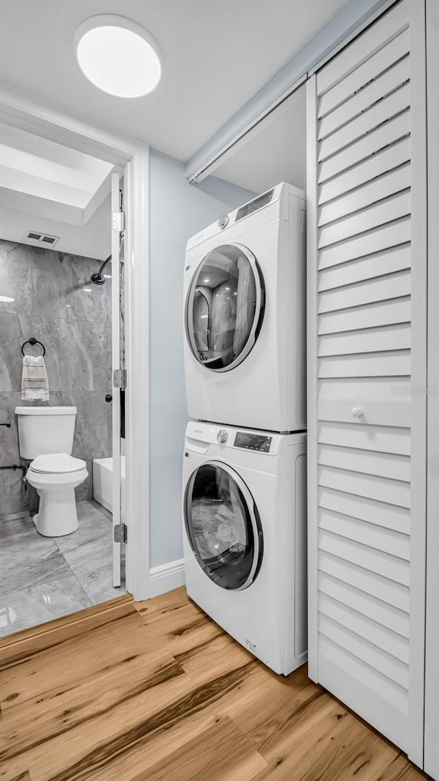 washroom featuring laundry area, stacked washing maching and dryer, wood finished floors, and visible vents