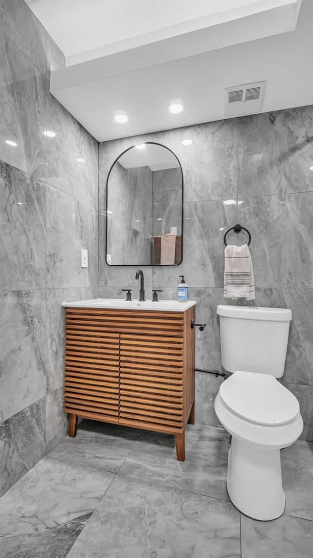 bathroom with toilet, tile walls, visible vents, and vanity
