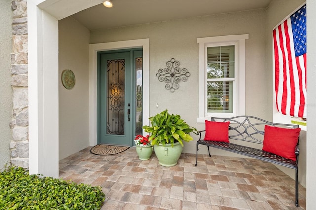 view of exterior entry with stucco siding, a porch, and stone siding