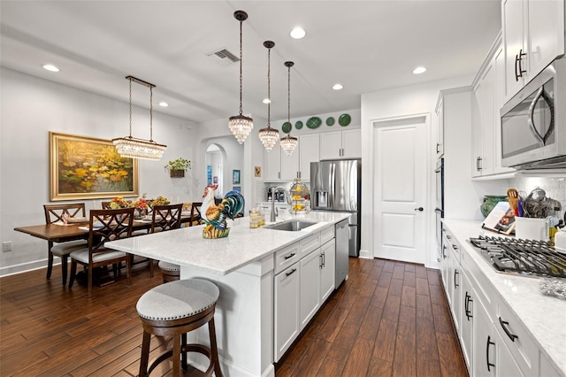 kitchen with arched walkways, dark wood finished floors, a sink, a breakfast bar, and stainless steel appliances