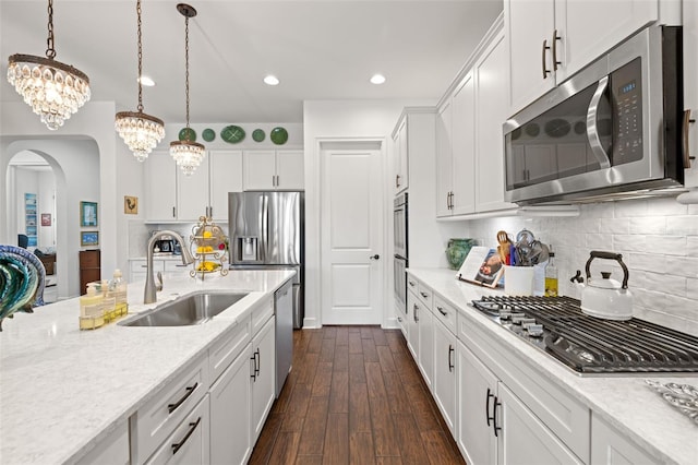 kitchen with a notable chandelier, appliances with stainless steel finishes, a sink, arched walkways, and white cabinetry