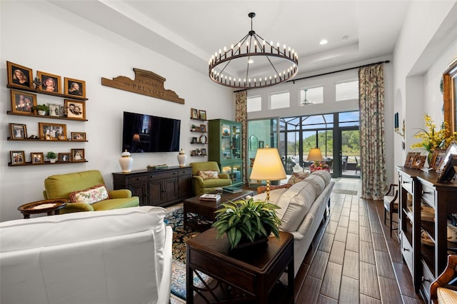 living room with a towering ceiling, recessed lighting, dark wood-type flooring, a raised ceiling, and a notable chandelier