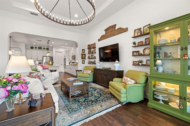 living room featuring a notable chandelier, a raised ceiling, arched walkways, visible vents, and dark wood-style floors