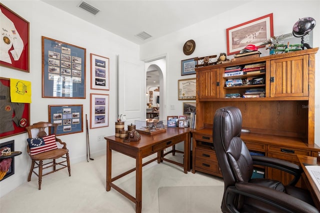 home office with arched walkways, visible vents, and light carpet