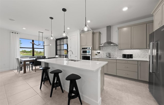 kitchen featuring gray cabinets, backsplash, appliances with stainless steel finishes, a sink, and wall chimney exhaust hood
