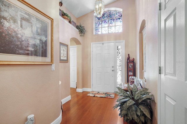 entrance foyer with arched walkways, a high ceiling, baseboards, and wood finished floors