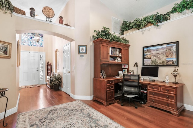office area featuring arched walkways, baseboards, and wood finished floors