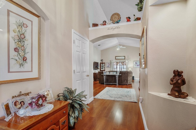 hall featuring wood finished floors, arched walkways, baseboards, and lofted ceiling