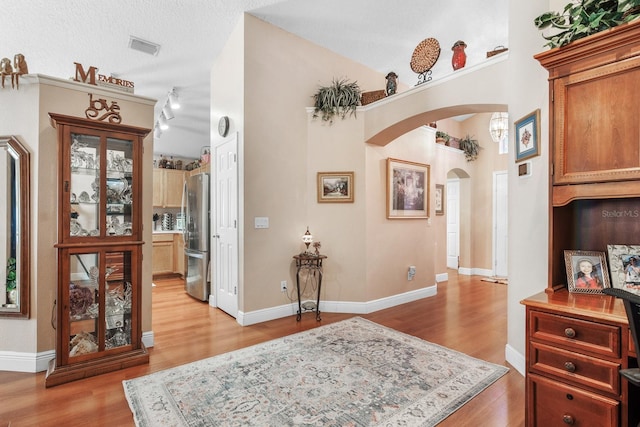 hall featuring arched walkways, visible vents, lofted ceiling, and light wood-type flooring