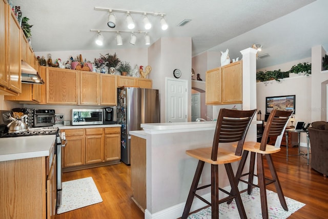 kitchen with wall chimney exhaust hood, appliances with stainless steel finishes, wood finished floors, and a breakfast bar area