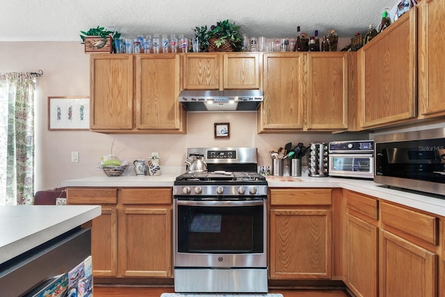 kitchen featuring exhaust hood, a textured ceiling, light countertops, a toaster, and stainless steel appliances