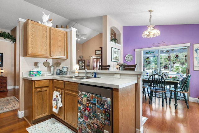 kitchen with vaulted ceiling, wood finished floors, a sink, light countertops, and dishwashing machine