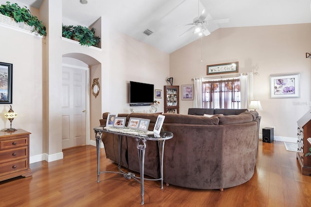 living area with a ceiling fan, wood finished floors, baseboards, high vaulted ceiling, and arched walkways