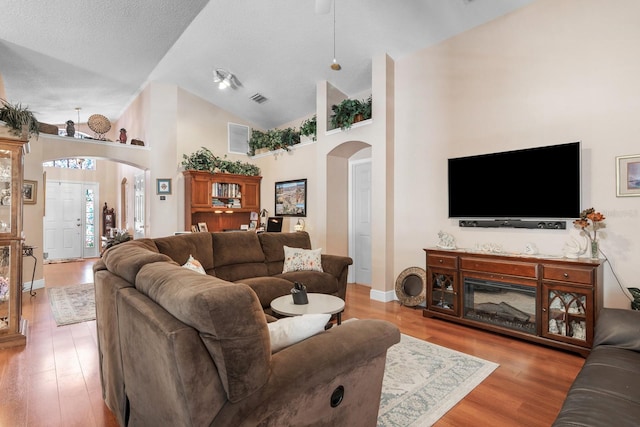 living room with arched walkways, high vaulted ceiling, a textured ceiling, wood finished floors, and visible vents