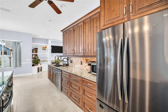 1424 Ridge Shore Dr, Tarpon Springs, FL 34689 - kitchen featuring appliances with stainless steel finishes, a ceiling fan, light stone countertops, tasteful backsplash, and brown cabinets