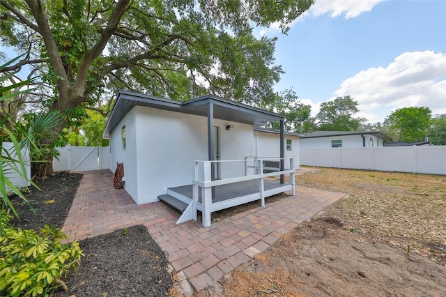 rear view of house featuring a patio, fence, a gate, and stucco siding