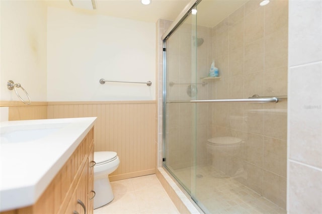 bathroom featuring tile patterned flooring, vanity, wainscoting, toilet, and a stall shower