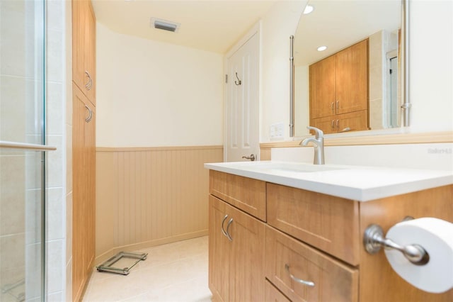 bathroom with a shower with shower door, vanity, tile patterned floors, a wainscoted wall, and visible vents