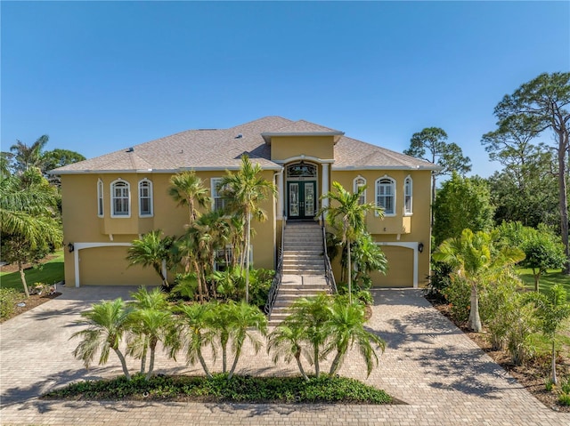 mediterranean / spanish home with decorative driveway, stucco siding, french doors, an attached garage, and stairway
