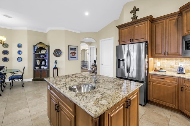 kitchen with arched walkways, tasteful backsplash, a sink, stainless steel appliances, and an island with sink