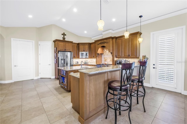 kitchen featuring decorative backsplash, brown cabinetry, appliances with stainless steel finishes, vaulted ceiling, and light stone counters
