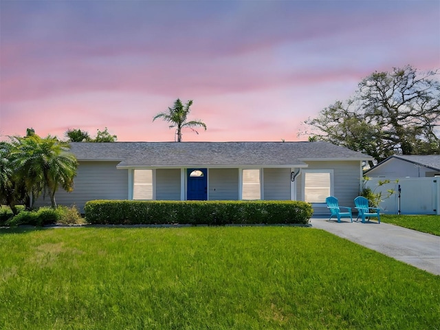 ranch-style home featuring a yard, roof with shingles, and fence
