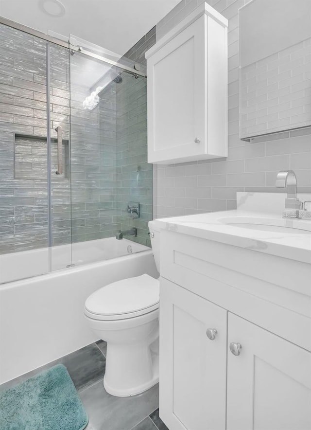 bathroom featuring toilet, tile walls, backsplash, bath / shower combo with glass door, and vanity