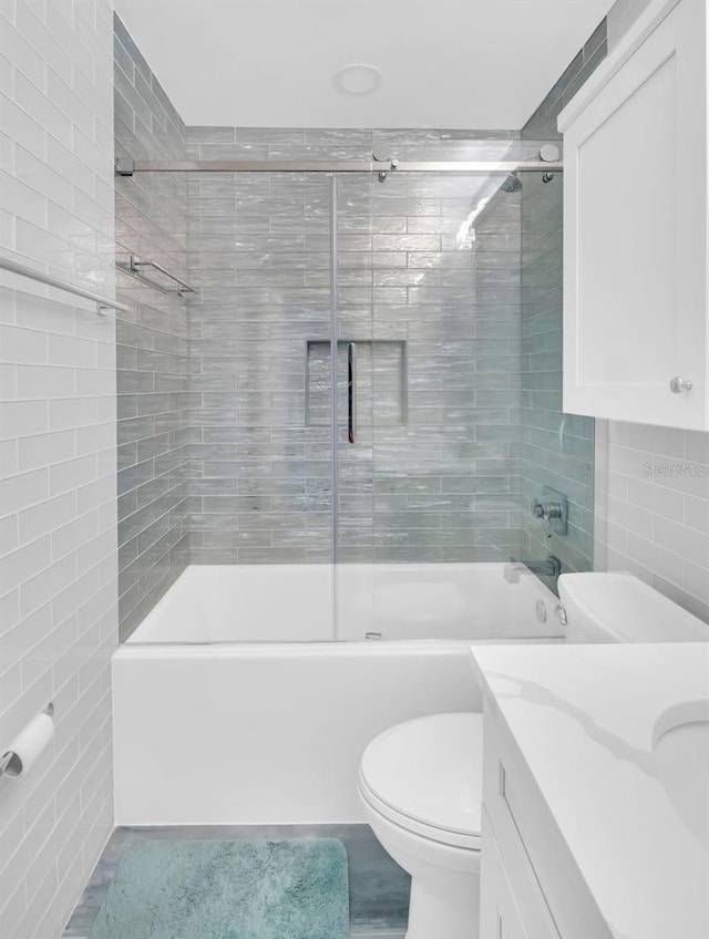 full bath featuring toilet, tile walls, vanity, and enclosed tub / shower combo
