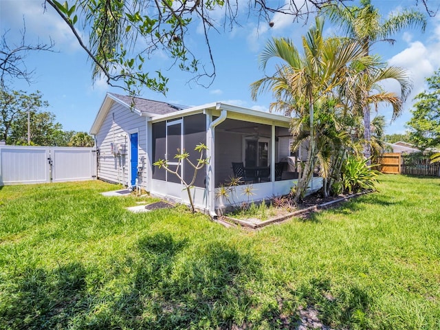 rear view of house with a lawn, a sunroom, a fenced backyard, and a gate