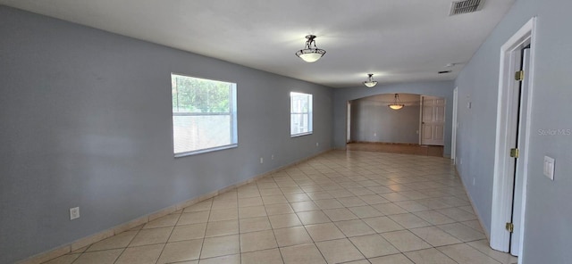 unfurnished room featuring arched walkways, baseboards, visible vents, and light tile patterned flooring