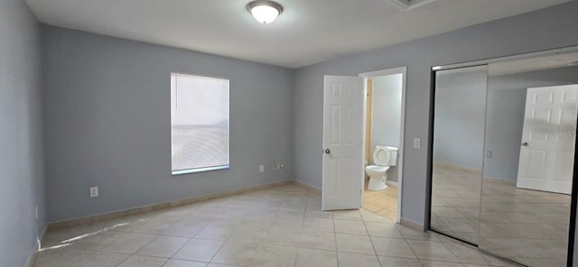 unfurnished bedroom featuring light tile patterned floors, baseboards, a closet, and connected bathroom