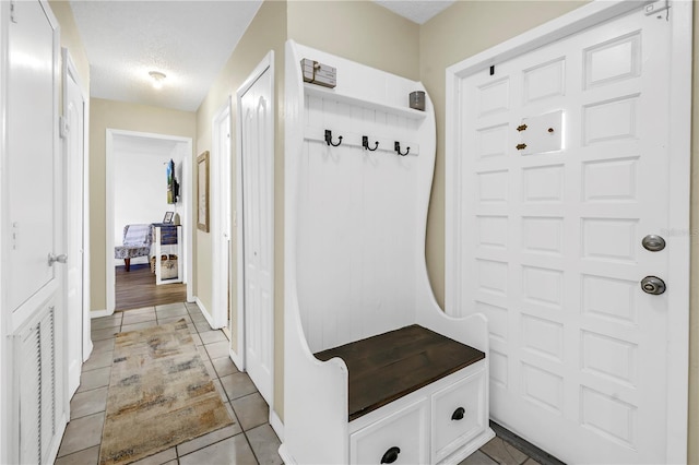 mudroom with baseboards, a textured ceiling, and light tile patterned floors